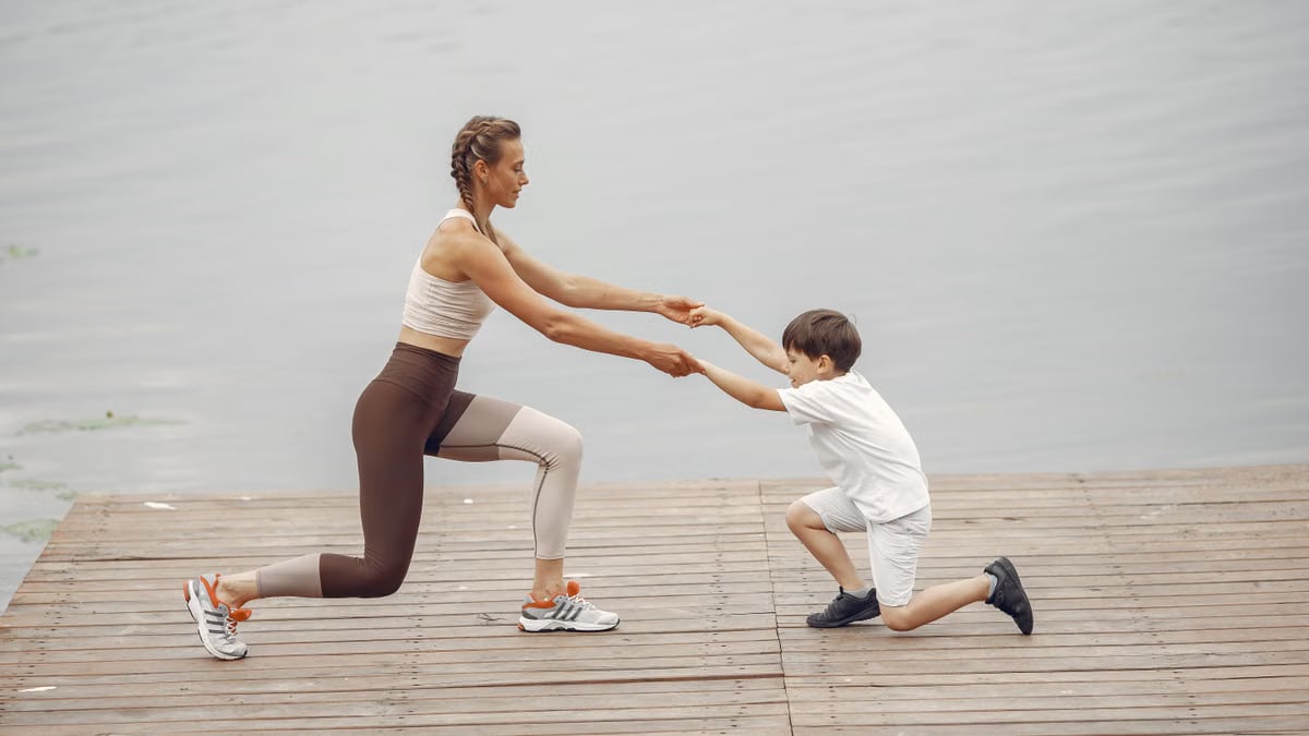 A woman and a boy exercise together on a wooden deck by the lake, promoting healthy lifestyle.